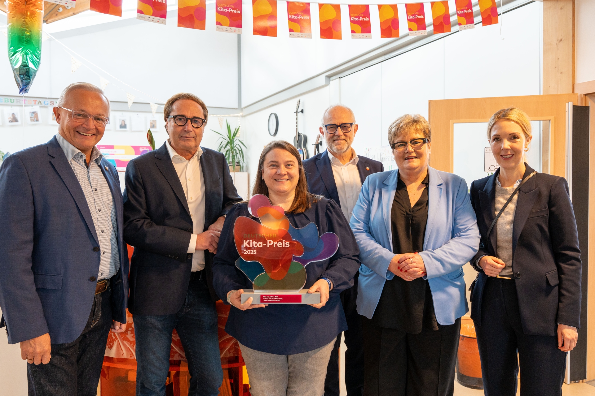 Gemeinsam mit der Staatssekretärin im rheinland-pfälzischen Bildungsministerium, Bettina Brück, der Bundestagsabgeordneten Ellen Demuth, Stadtbürgermeister Alfons Mußhoff und dem Geschäftsführer des gemeinnützigen Betreibergesellschaft HTZ Neuwied, Thomas Voß, gratulierte Landrat Achim Hallerbach der inklusiven städtischen Kita Unkel und Leiterin Claudia Gries zum Titel „Beste Kita des Jahres 2025 in ganz Deutschland“. Foto: Martin Boden / Kreisverwaltung Neuwied