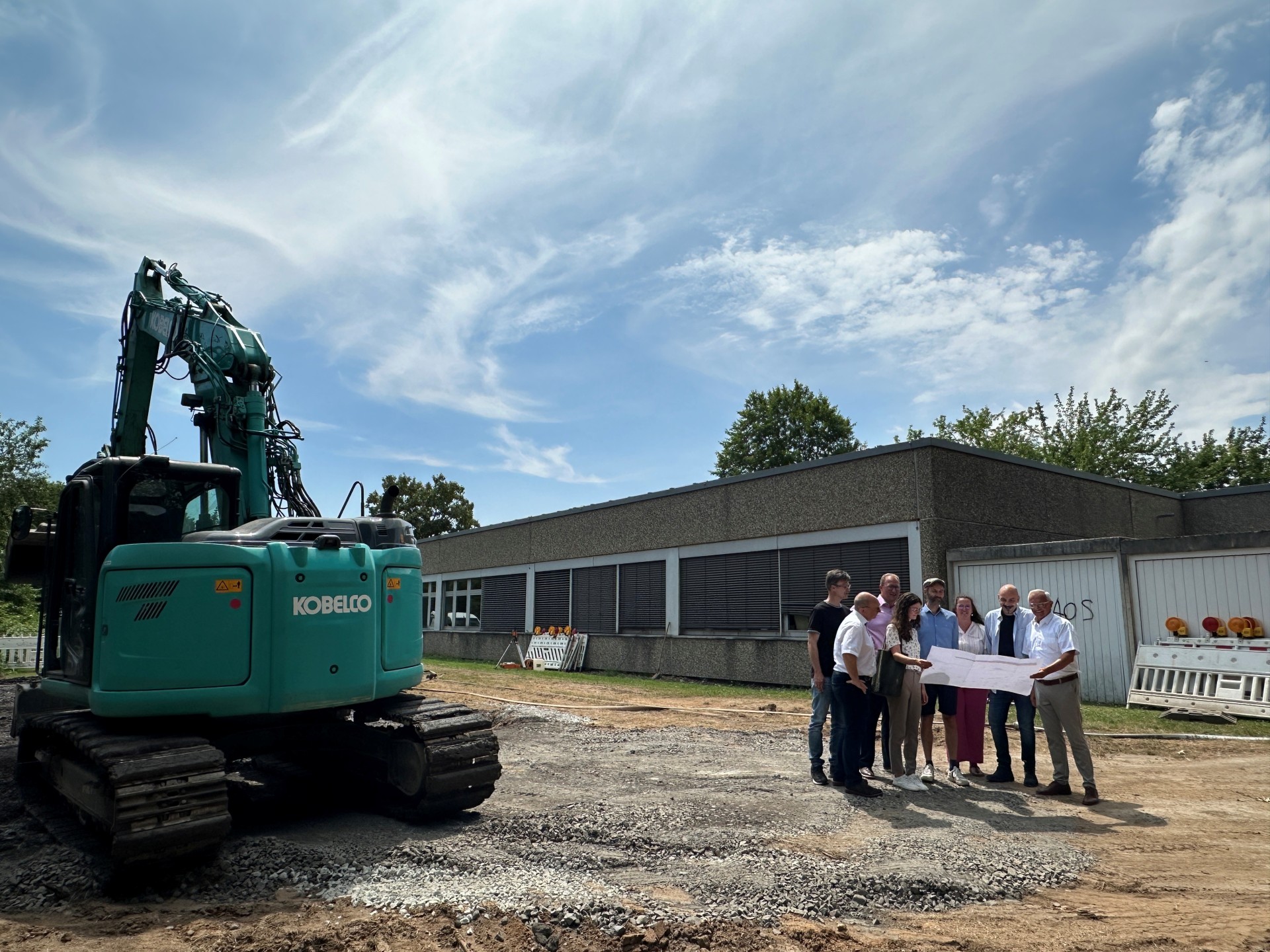 Mit ausreichend Sicherheitsabstand zum Bagger beobachten Landrat Achim Hallerbach, der 1. Kreisbeigeordnete Phillip Rasbach sowie der stellvertretende Abteilungsleiter Schulen, Dirk Arenz, Christina Junk und Marco Müller vom Kreis-Immobilienmanagement, flankiert von Dr. Tibor Fülöpp und Stephanie Brand (Rektor und Konrektorin Max-Kolbe-Schule) und Marco Cicoria (Konrektor Realschule) die Bauarbeiten an der Römerwall-Schule in Rheinbrohl. Foto: Thomas Herschbach