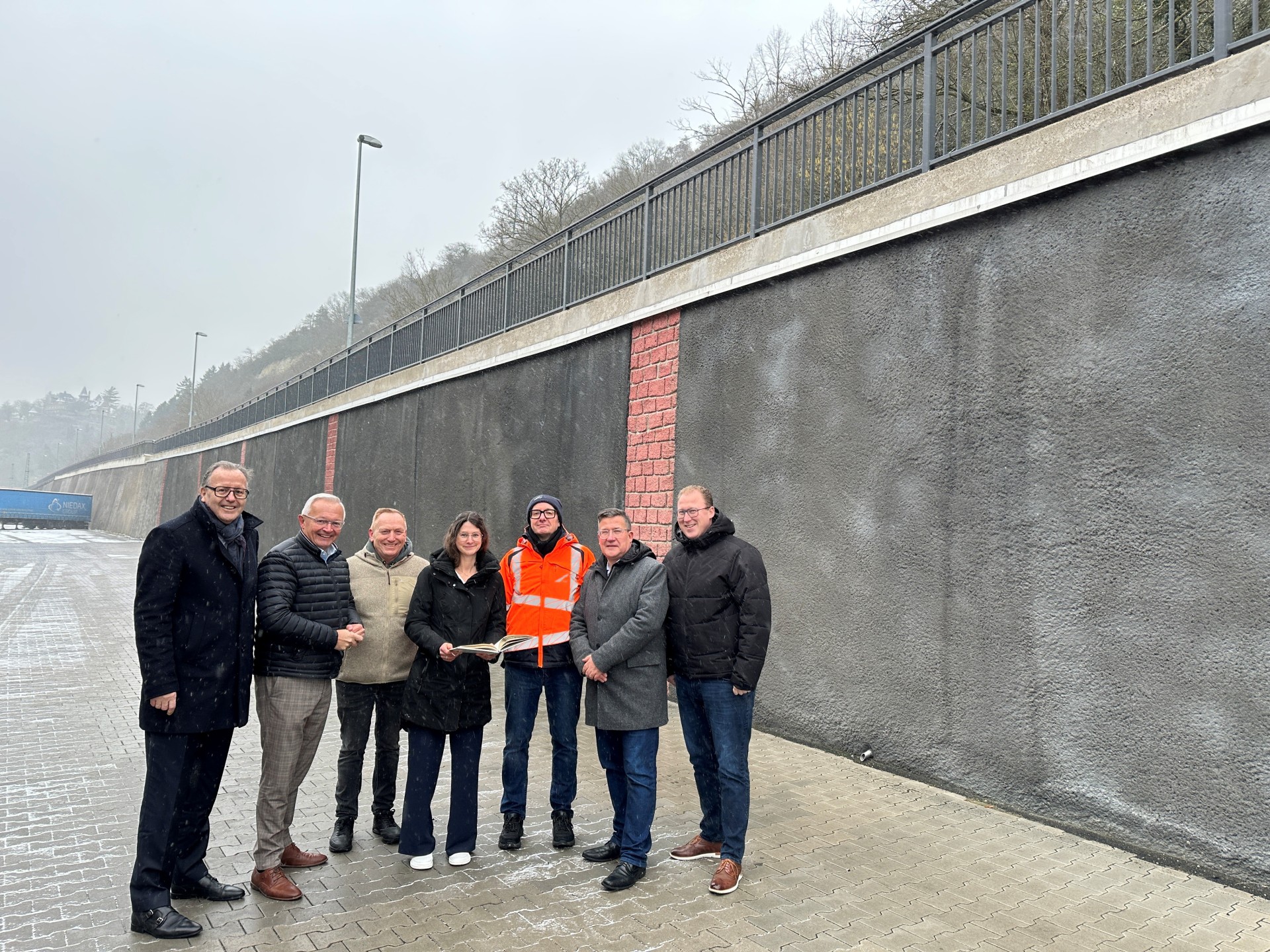 Trotz winterlichem Schneegestöber machten sich Landrat Achim Hallerbach, der 1. Kreisbeigeordnete Phillip Rasbach, der Bürgermeister der Verbandsgemeinde Linz, Frank Becker, und Stadtbürgermeister Helmut Muthers ein Bild vom Ergebnis der Bauarbeiten an der Stützmauer entlang der K 11. Auf den Stand der Dinge ließ sich das Quartett der Verwaltungsspitzen von LBM Bauaufseher Reiner Lahr und Christina Junk vom Kreis-Immobilienmanagement bringen. Foto: Thomas Herschbach