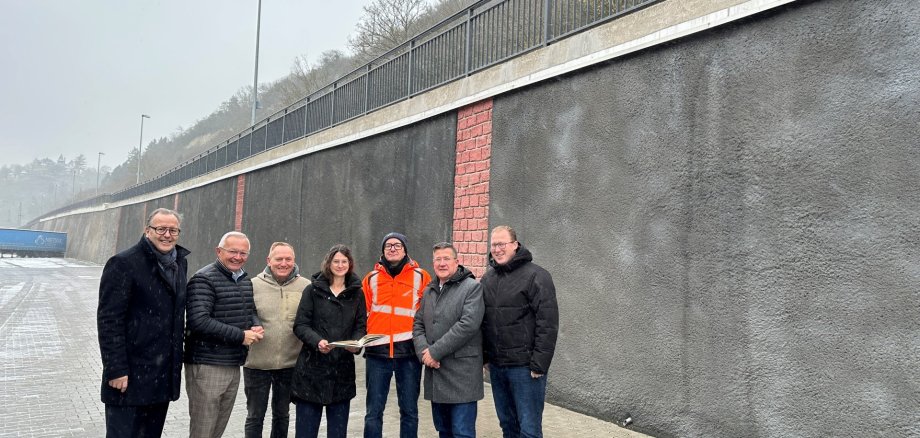 Trotz winterlichem Schneegestöber machten sich Landrat Achim Hallerbach, der 1. Kreisbeigeordnete Phillip Rasbach, der Bürgermeister der Verbandsgemeinde Linz, Frank Becker, und Stadtbürgermeister Helmut Muthers ein Bild vom Ergebnis der Bauarbeiten an der Stützmauer entlang der K 11. Auf den Stand der Dinge ließ sich das Quartett der Verwaltungsspitzen von LBM Bauaufseher Reiner Lahr und Christina Junk vom Kreis-Immobilienmanagement bringen. Foto: Thomas Herschbach