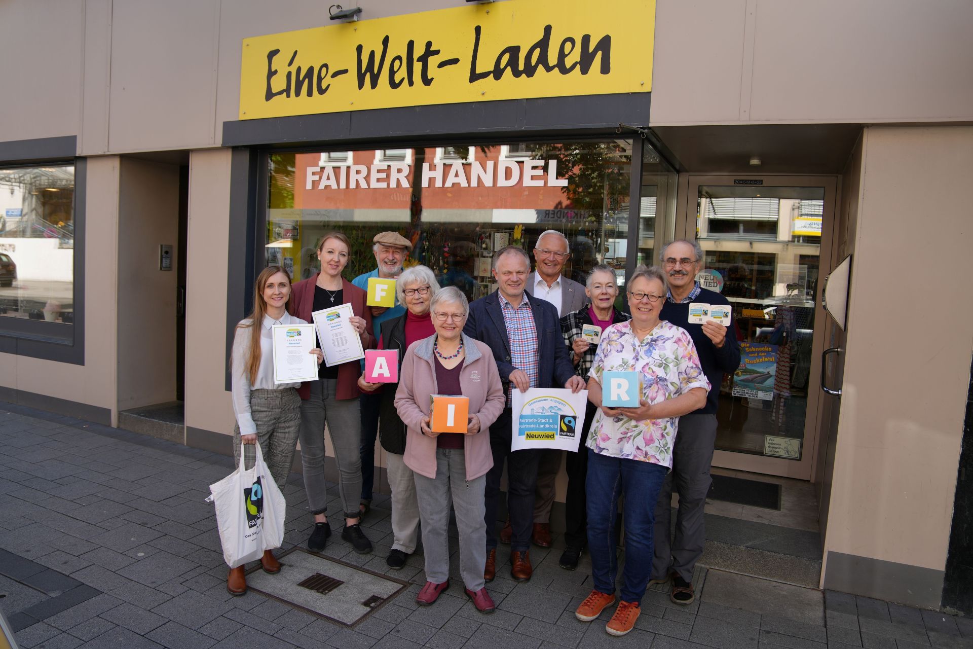 Vor dem Eine-Welt-Laden in der Neuwieder Innenstadt freuen sich Oberbürgermeister Jan Einig, Landrat Achim Hallerbach, die Steuerungsgruppen der Fairtrade-Stadt Neuwied sowie Ehrenamtliche des Eine-Welt-Ladens, dass der Fairtrade-Town-Titel verlängert wurde. Foto: Nadine Schöneberg / Stadtverwaltung Neuwied