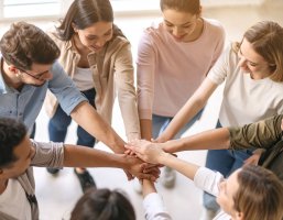Viele Personen stehen im kreis und strecken eine Hand aus um Zusammenhalt und Stärke zu symbolisieren.