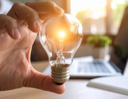 Eine Hand die zwischen Zeigefinger und Daumen eine Glühbirne hält.