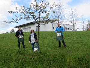 Foto: Ortsbürgermeister Achim Braasch (von links), Gabi Schäfer und Landrat Achim Hallerbach haben den ersten Bewässerungssack einem jungen Baum in Oberraden umgelegt. 