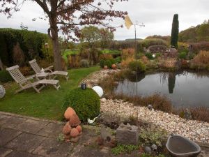 Foto: Ein großer Naturteich, zahlreiche Gehölze und viele unterschiedliche Sitzplätze mit natürlichen Baumaterialen und Steinskulpturen kennzeichnen den eher ruhig und in vielen Grüntönen gehaltenen Garten.