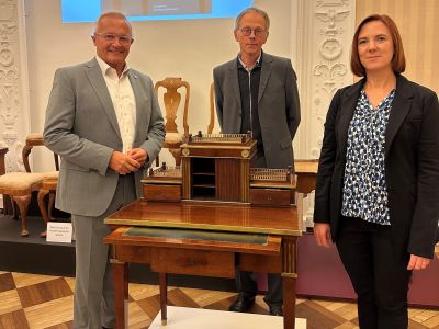 Bild: Museumsleiterin Jennifer Stein, Kurator Dr. Achim Stiegel und Landrat Achim Hallerbach freuen sich, dass mit dem klassizistischen Damenschreibtisch aus der Werkstatt von Johann David Hacker die renommierte Sammlung an Roentgen-Möbeln und Kinzing-Uhren um ein neues Glanzstück erweitert werden konnte. Foto: Thomas Herschbach
