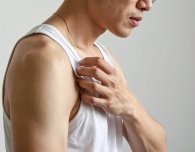 Junger Mann kratzt sich am Arm.