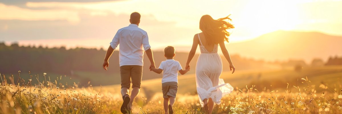 Vater, Mutter, Kind laufen in der Abenddämmerung über eine Weide.