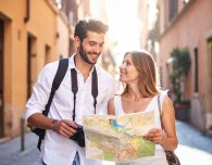 Nahaufnahme eines Pärchen, in einem Urlaubsort. Beide halten eine Stadtkarte in der Hand. Der Mann hat eine Kamera umgehangen.