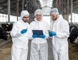 Personen in weißen Schutzanzügen, die alle auf ein Smart-Tablet schauen.