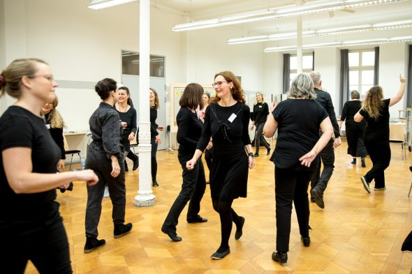 Schwarz gekleidete Personen gehen quer durcheinander in einem Saal.