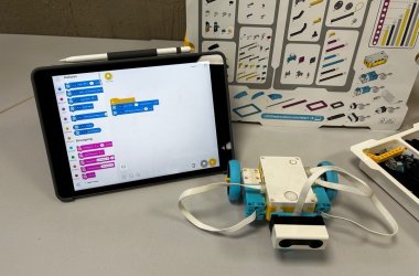 Auf einem Tisch stehen die Utensilien für Lego-Spike: Tablet, Plan mit den einzelen Legobausteinen, Legobausteine und das Anfangsmodell für den Roboter.