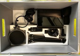 Eine Kiste ist zu sehen, in der die Untensilien für einen Podcast sind: Kopfhörer, Stativ, Mikrofon, Tablet.