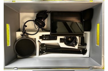 Eine Kiste ist zu sehen, in der die Untensilien für einen Podcast sind: Kopfhörer, Stativ, Mikrofon, Tablet.